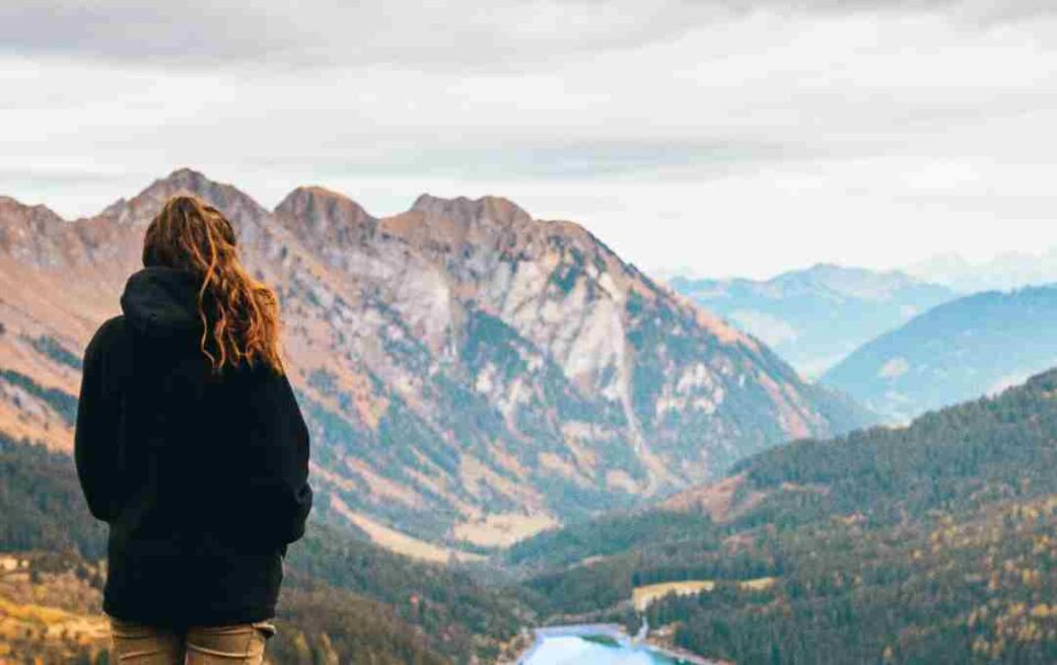 Frau steht auf einem Berg und blickt in die Weite über einen See – Symbol für innere Stärke, Resilienz und Gelassenheit in stürmischen Zeiten.